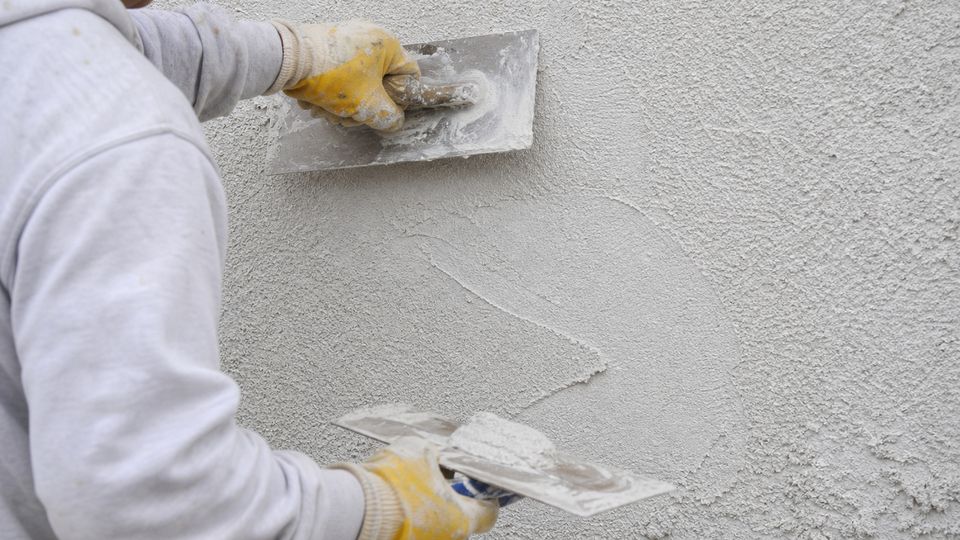Maler zieht mit zwei Gl&auml;ttkellen Reibeputz an einer Wand ab